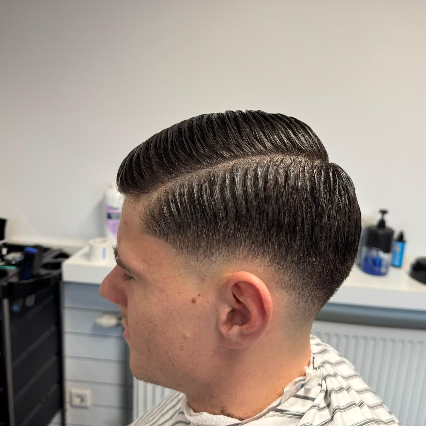 Skin fade met een scherpe scheiding, van opzij gezien in de zaak