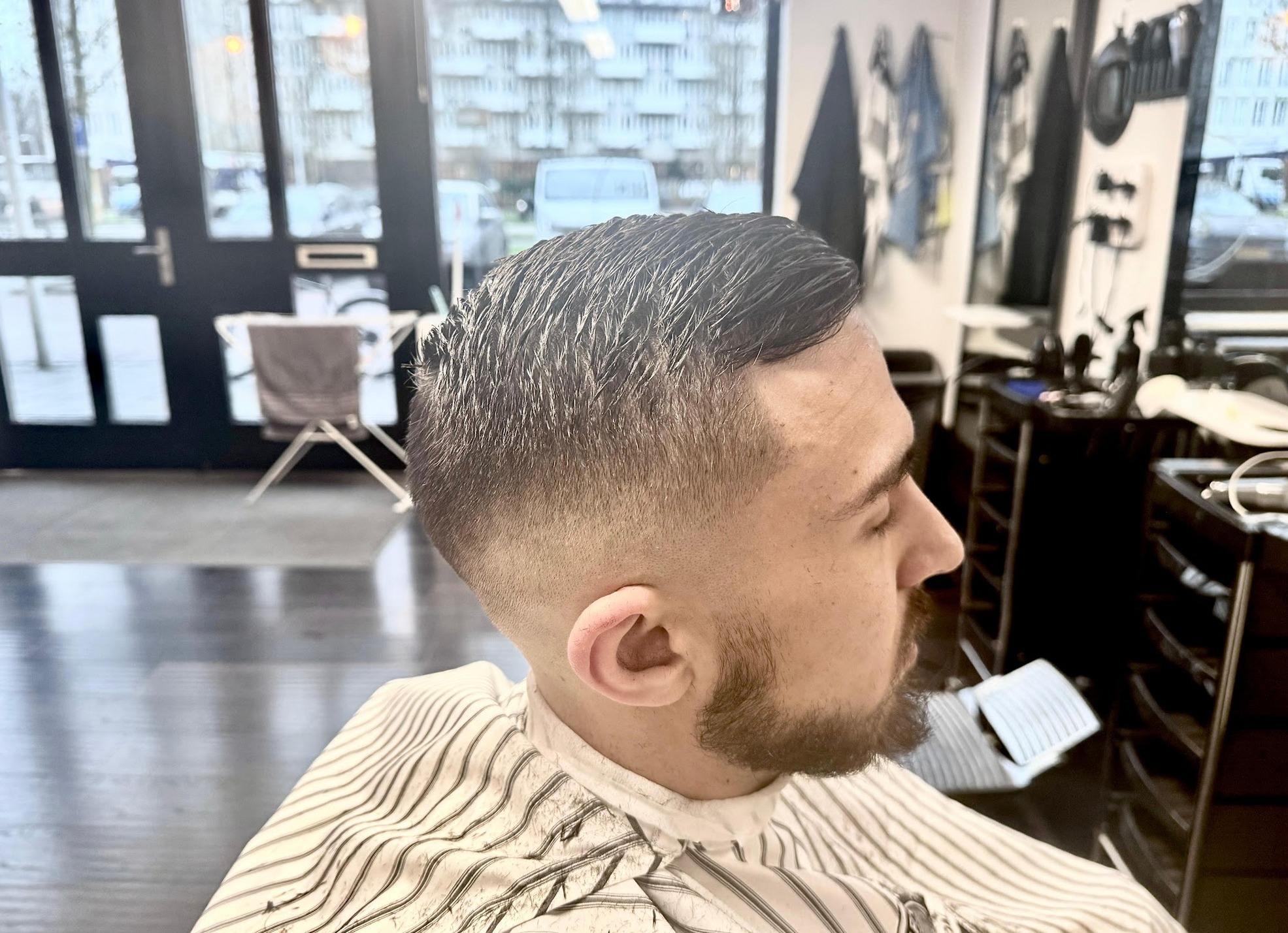 Fade met baard in de stoel, de ramen van de zaak op de achtergrond